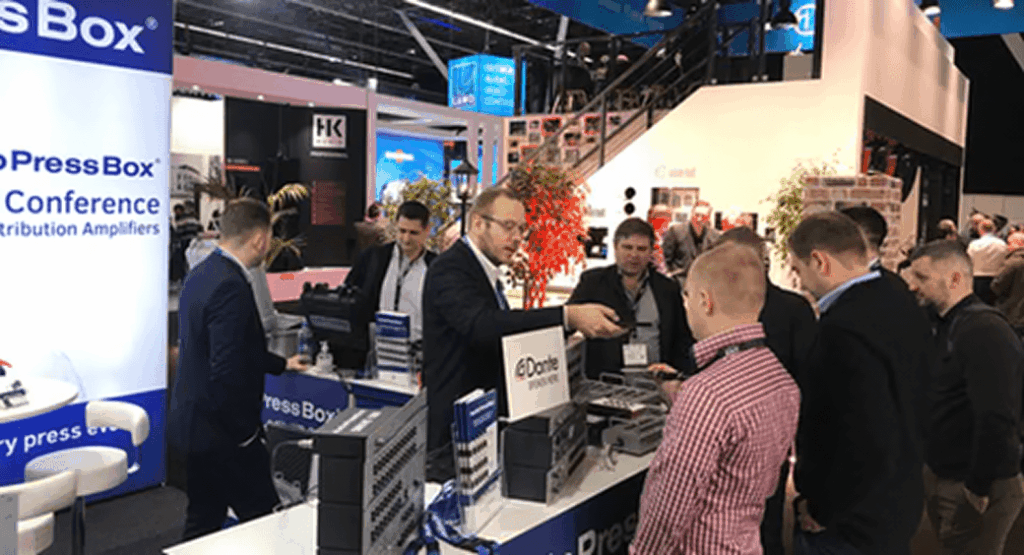 AudioPressBox trade show booth demonstration — visitors discussing press box audio distribution